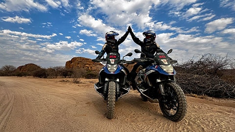 Twee motorrijdsters van het Franse damesteam zitten naast elkaar op hun R 1300 GS Competition Bikes en geven elkaar een high five.