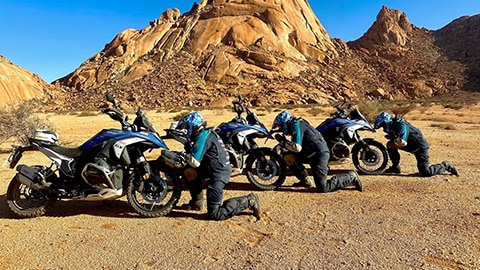 De drie coureurs van het Indiase herenteam knielen voor hun motoren.