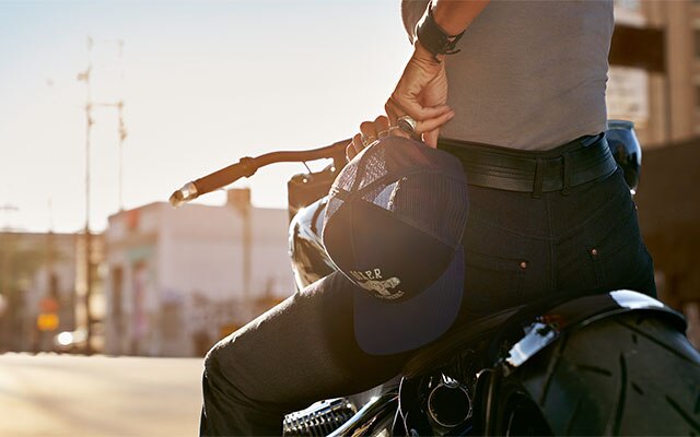 Een motorrijdster heeft in de ingezoomde foto de Cap Boxer uit de collectie in haar hand en draagt de jeans RoadCrafted voor dames.