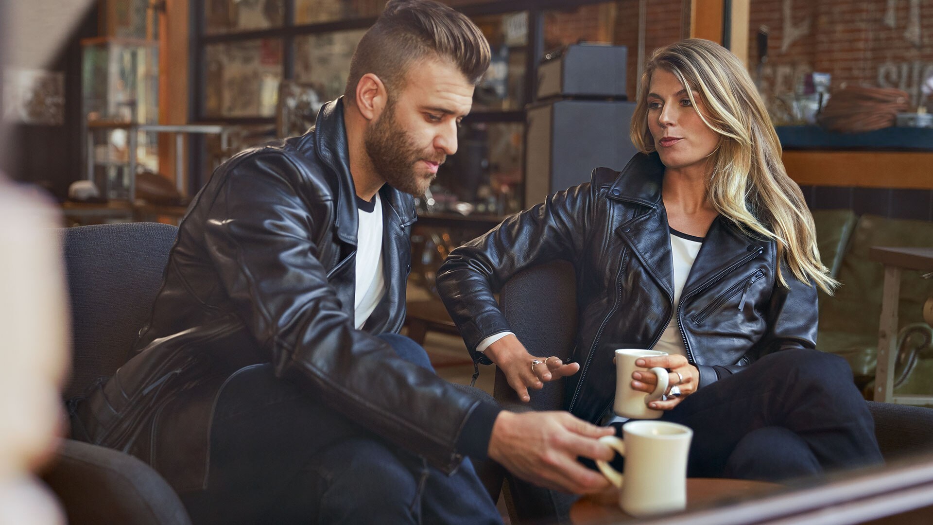 Op de foto zitten een jonge man in het leren jack FlatTwin voor heren en een jonge vrouw in het leren jack FlatTwin voor dames tegenover elkaar.