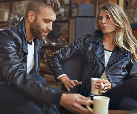 Op de foto zitten een jonge man in het leren jack FlatTwin voor heren en een jonge vrouw in het leren jack FlatTwin voor dames tegenover elkaar.