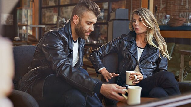 Op de foto zitten een jonge man in het leren jack FlatTwin voor heren en een jonge vrouw in het leren jack FlatTwin voor dames tegenover elkaar.